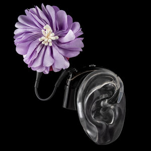 Black ear mould shows cochlear implant with coil hat in a lilac flower design